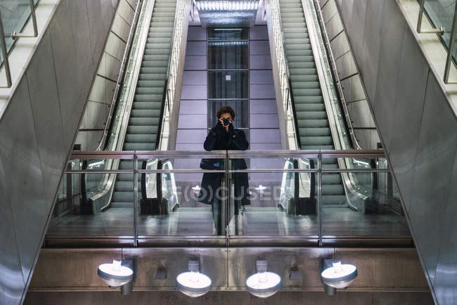 Front view of man taking photo with camera on background of moving stairs — Stock Photo