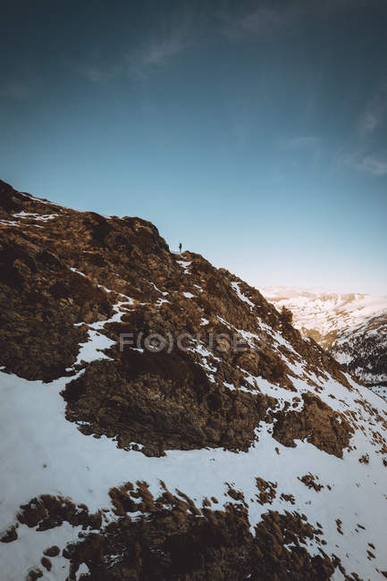 Distant view of tourist standing on picturesque snowy mountain slope on background of idyllic skyscape — Stock Photo