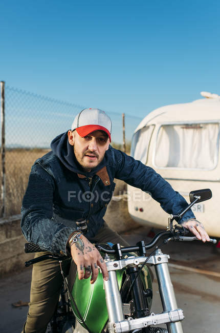 Porträt eines Mannes mit Mütze posiert an sonnigen Tagen auf einem Motorrad in der Nähe von Lieferwagen — Stockfoto