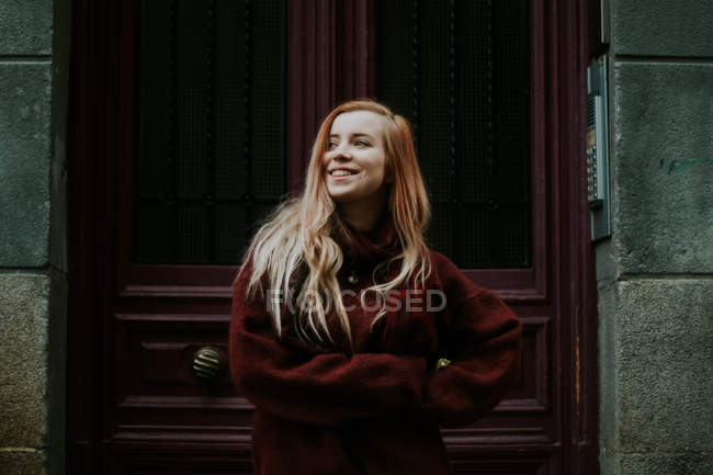 Femme blonde souriante debout sur le fond de la porte en bois . — Photo de stock
