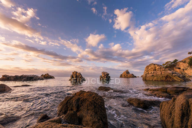 Rocky costa oceanica sotto nuvoloso paesaggio luminoso in cielo — Foto stock