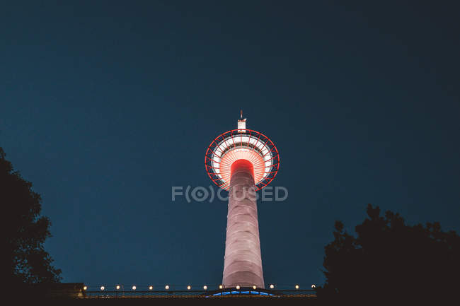 De baixo vista para a torre iluminada sobre céu noturno no fundo — Fotografia de Stock
