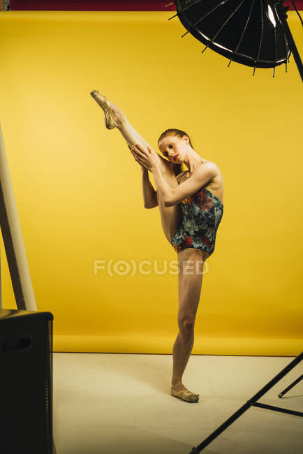 Dançarina de balé segurando perna levantada sobre fundo amarelo — Fotografia de Stock