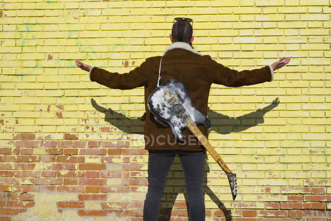 Rear view of man with old guitar on back at street scene — Stock Photo