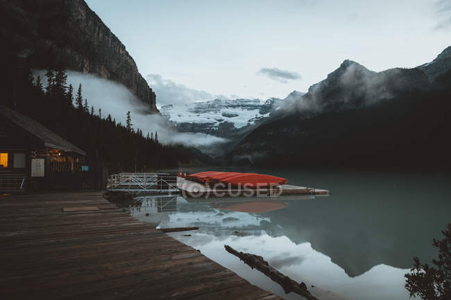 Дерев'яний будинок в джуті з човнами на спокійному гірському озері — стокове фото