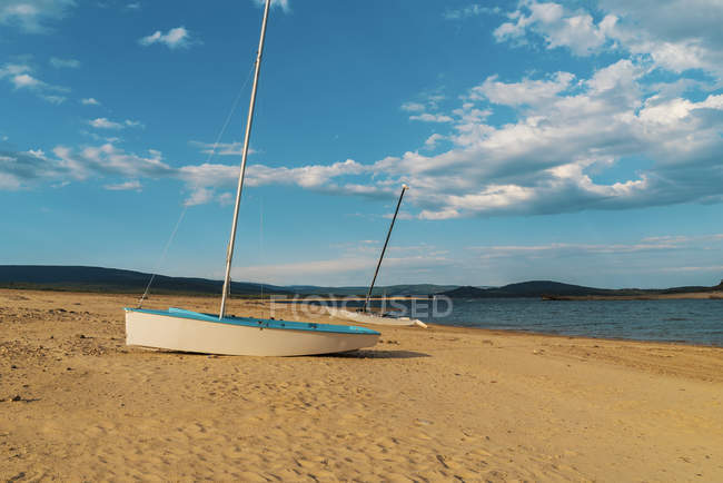 Small vessel placed on sandy shore at lake in sunny day. — Stock Photo