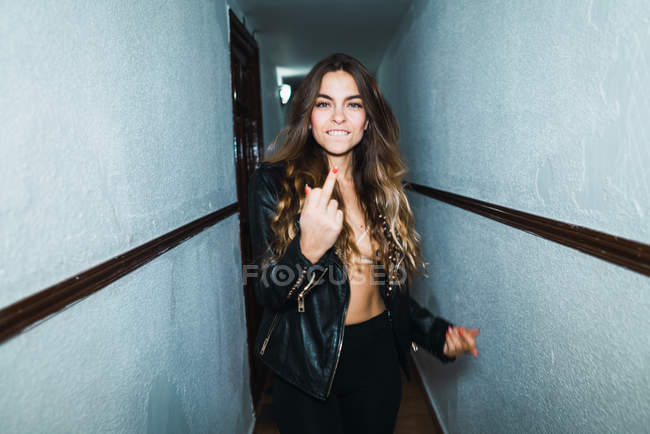 Cheerful woman walking in corridor and showing middle finger at camera — Stock Photo