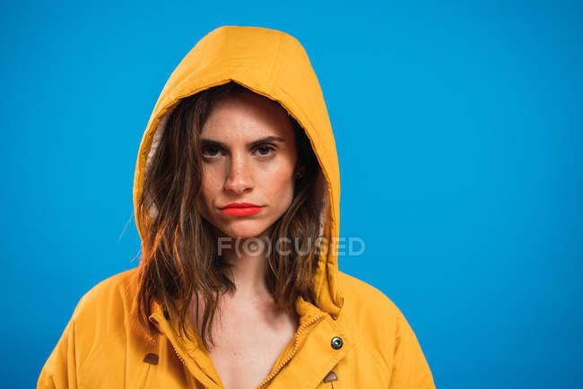 Женщина в жёлтом капюшоне позирует на синем фоне — стоковое фото