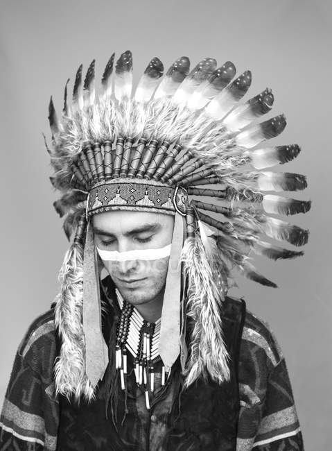 Joven con la línea en la cara posando en traje tradicional nativo americano en el estudio - foto de stock