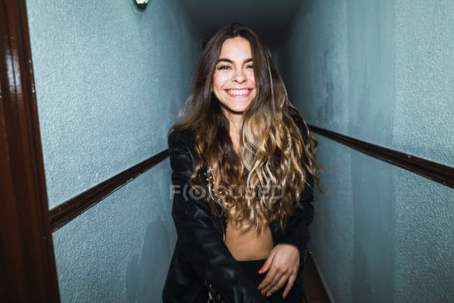 Mujer alegre en chaqueta sonriendo y posando en pasillo . - foto de stock