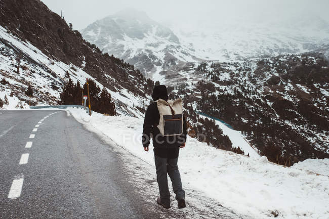 Вид сзади на человека, идущего по снежной дороге в горах — стоковое фото