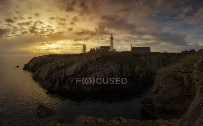 Distant view of coastal cliff with lighthouse over sunset sky — Stock Photo
