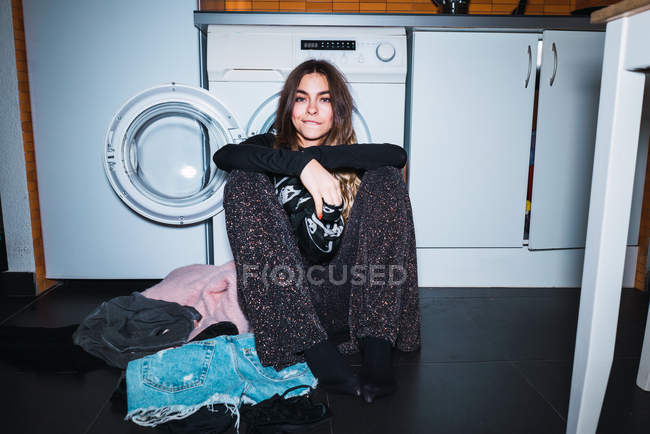 Молода жінка сидить на підлозі і спирається на пральну машину вдома . — стокове фото