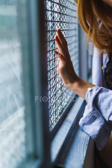 Crop redhead woman touching grid on window. — Stock Photo