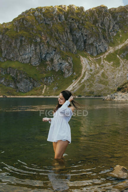 Smiling pretty woman standing in lake in hillside and touching hair. — Stock Photo