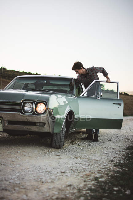 Homme monter dans une voiture vintage sur route de gravier — Photo de stock