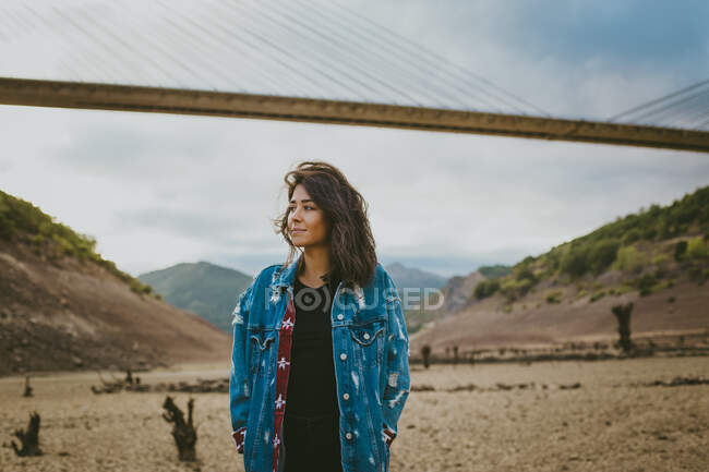 Young woman standing on background of bridge in hills and looking away. — Stock Photo