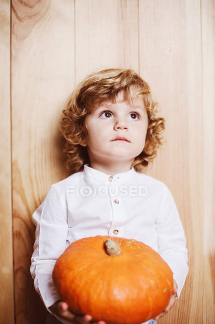 Adorable niño niño sosteniendo calabaza y mirando hacia arriba - foto de stock