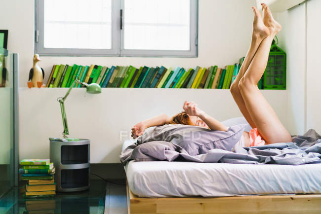 Frau liegt mit erhobenen Beinen im Bett — Stockfoto