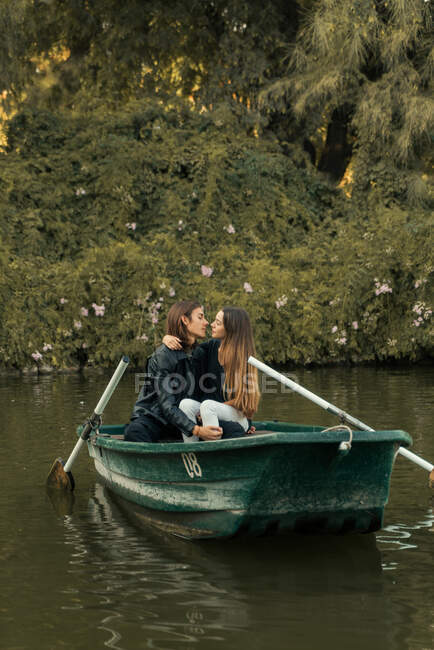 Jeune couple embrassant et regardant face à face dans le bateau dans la rivière contre les arbres verts. — Photo de stock