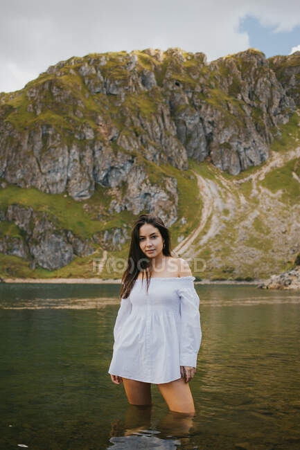 Sorrindo mulher bonita de pé no lago na encosta e tocando o cabelo. — Fotografia de Stock