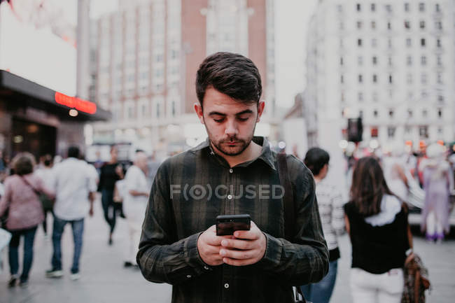Thoughtful man standing on city street and browsing smartphone. — Stock Photo