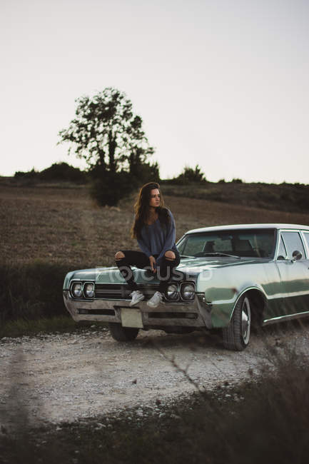 Молодая женщина сидит на винтажном автомобиле на природе — стоковое фото