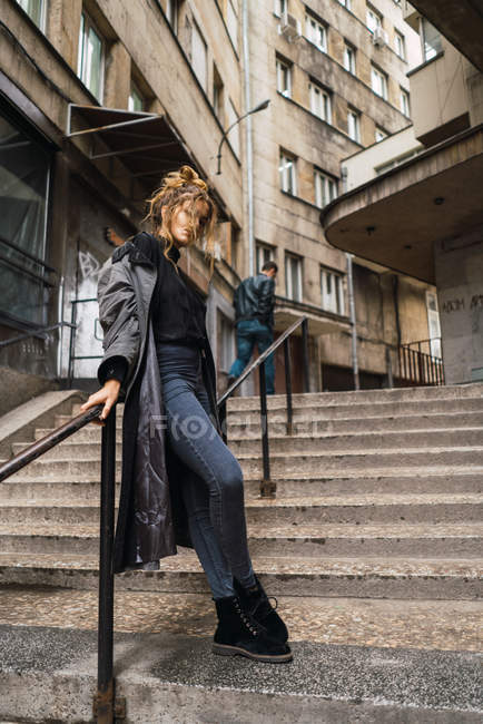Junge Frau in lässigem Mantel posiert im Treppenhaus auf der Straße. — Stockfoto