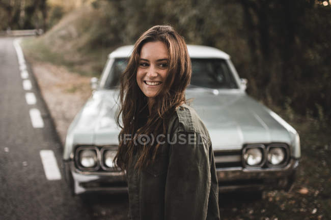 Усміхнена жінка стоїть на узбіччі біля ретро-автомобіля . — стокове фото