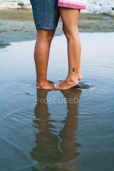 Sección baja de la pareja de pie en aguas poco profundas en la playa - foto de stock