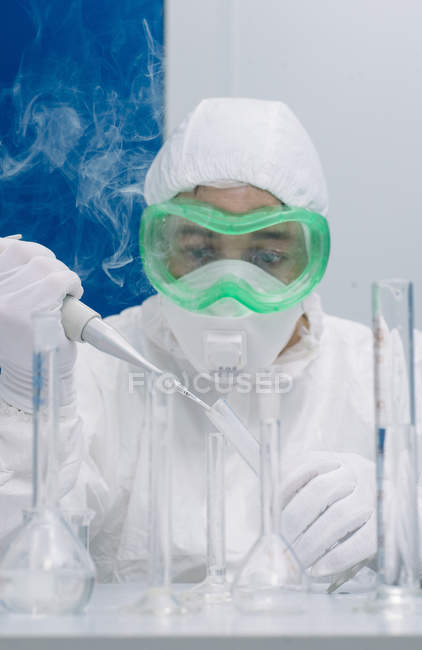Scientist pouring reagents with pipette to flasks while experiment — Stock Photo