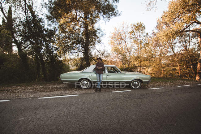 Selbstbewusster Mann lehnt am Kofferraum eines Autos am ruhigen Straßenrand — Stockfoto