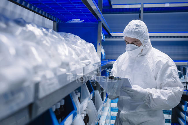 Cientista caminhando ao longo das prateleiras com reagentes e fornecendo revisão em laboratório — Fotografia de Stock