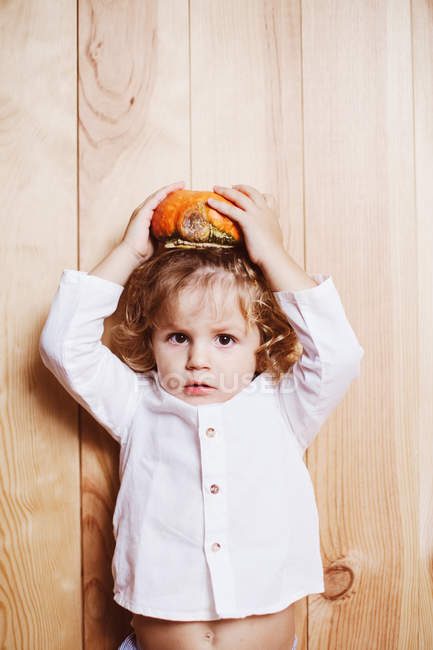 Adorable boy holding pumpkin on head and looking at camera — Stock Photo