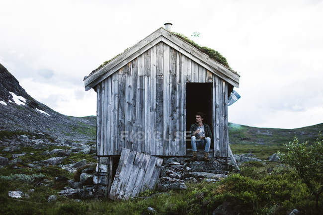 Человек, сидящий на пороге старого дома в природе — стоковое фото