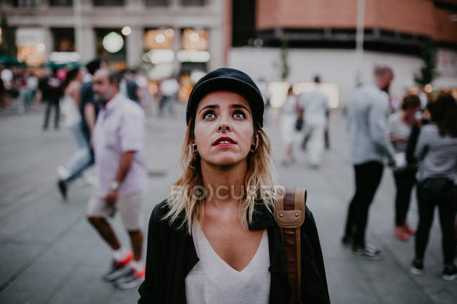 Retrato de mulher de boné preto em pé na rua e olhando para cima — Fotografia de Stock