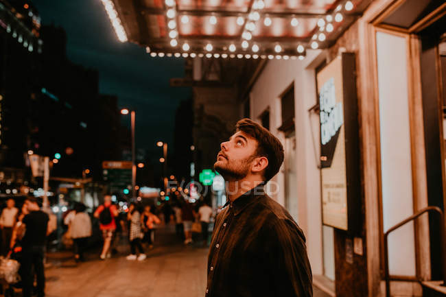 Hombre posando en la calle de la noche y mirando hacia arriba - foto de stock