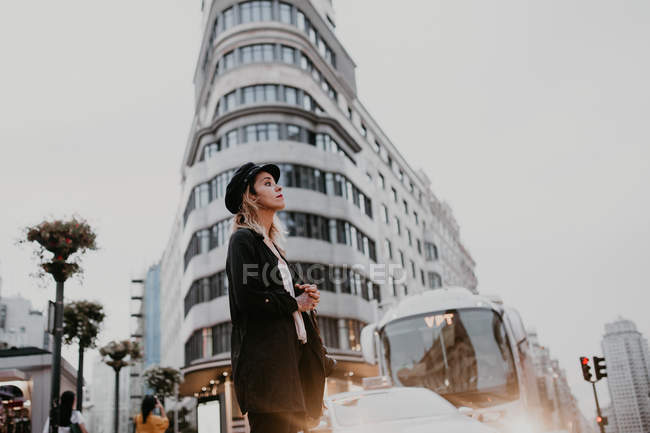 Vista lateral de la mujer en gorra negra caminando en la ciudad - foto de stock