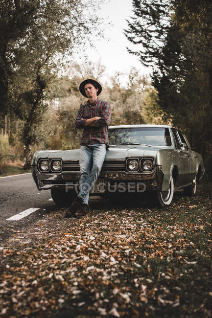 Confident young man with crossed arms leaning on trunk of retro car — Stock Photo