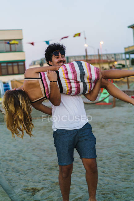 Счастливый мужчина гуляет с женщиной на руках на пляже — стоковое фото
