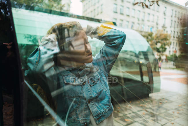 Shot through glass of young woman posing sensually behind glass of bus stop — Stock Photo