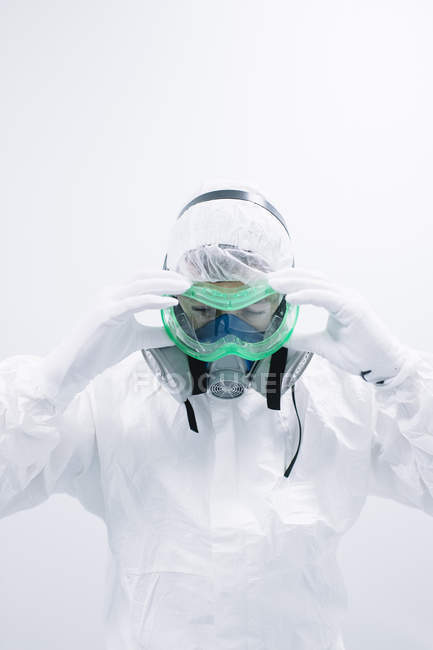 Científico en uniforme blanco poniéndose máscara protectora - foto de stock