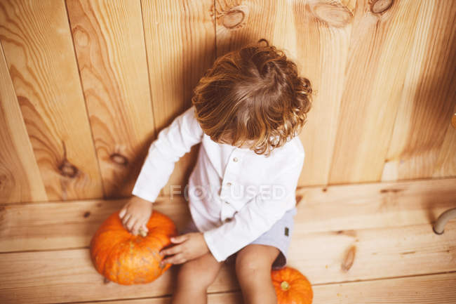 Kid sitting on floor and playing with pumpkin — Stock Photo