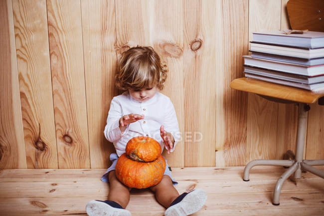 Encantador niño sentado en el suelo con calabazas apiladas en las rodillas - foto de stock