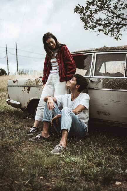 Young people leaning on old car, talking with each other and cheerfully smiling. — Stock Photo