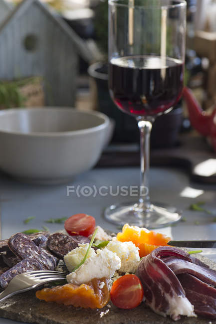 Tasty snacks on stone plate and glass of red wine — Stock Photo