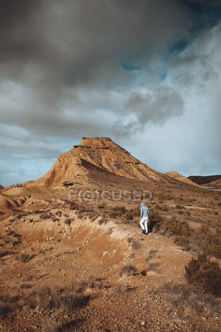 Vista posterior del hombre caminando a la colina de arena sobre hierba seca en día nublado . - foto de stock