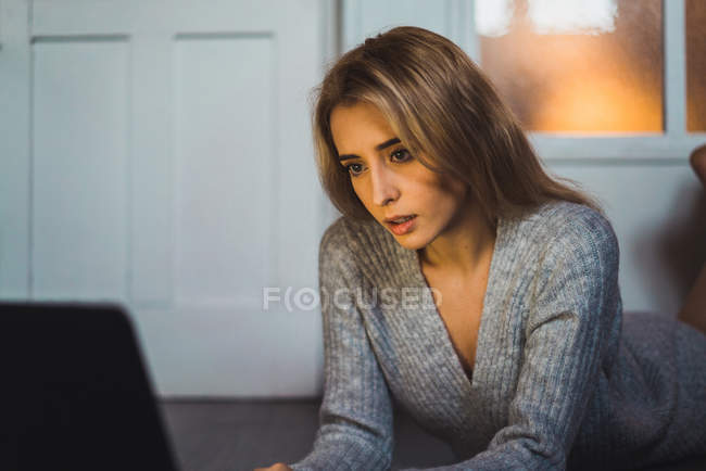 Женщина лежит на полу и использует ноутбук — стоковое фото