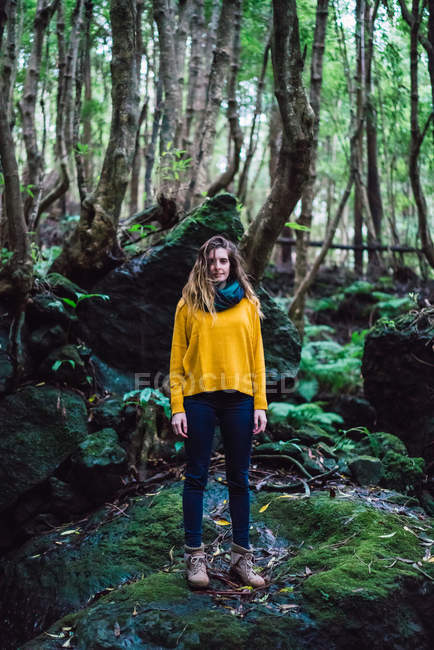 Jovem mulher pequena em pé na floresta verde e olhando para a câmera . — Fotografia de Stock