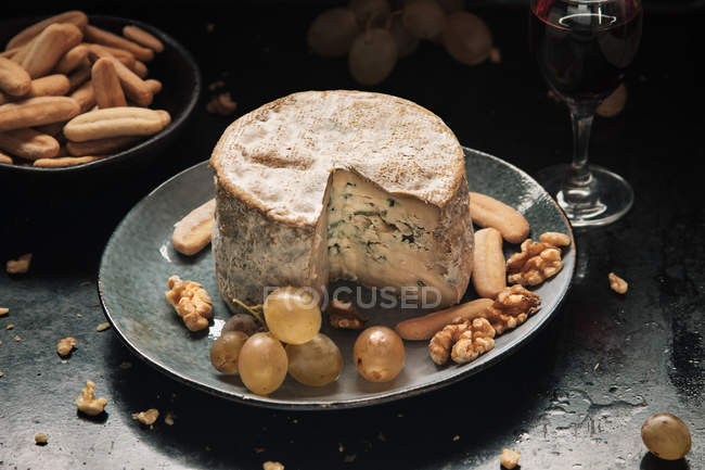 Cheese wheel with grapes on plate — Stock Photo